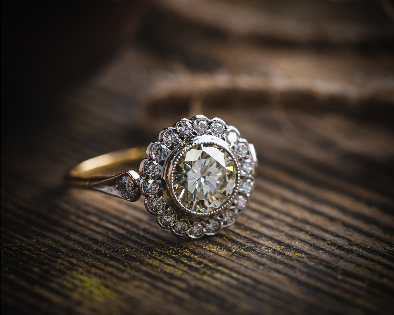 A large flower cluster diamond ring photographed on a wooden board with a piece of rope in the background.