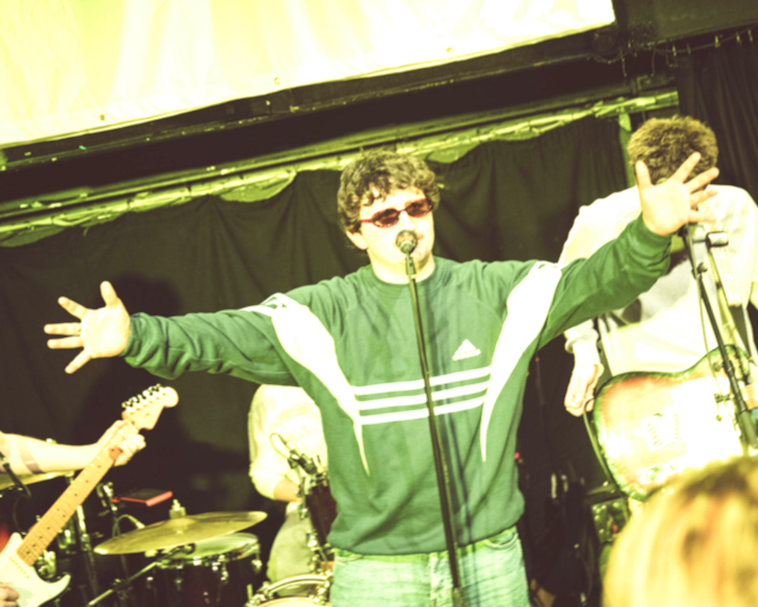 Park View playing at The Cluny 2 in Newcastle. Singer with arms outstretched, wearing a green Adidas sweatshirt, with musical instruments and another person in the background.
