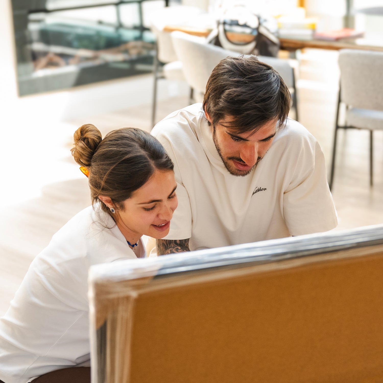 Sandro Tonali and Juliette Tonali in white shirts looking at a piece of paper in a modern indoor setting.