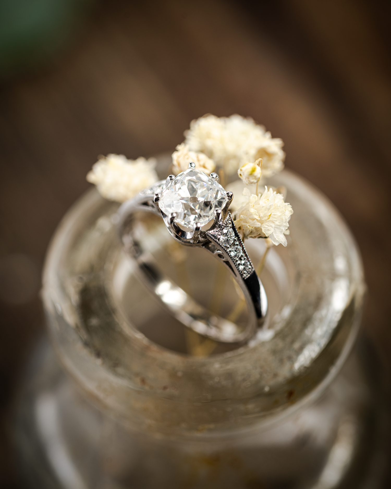 Large Old Cut Diamond Solitaire with Stone Set Shoulders photographed on top of an old medicine bottle, complete with dried flowers