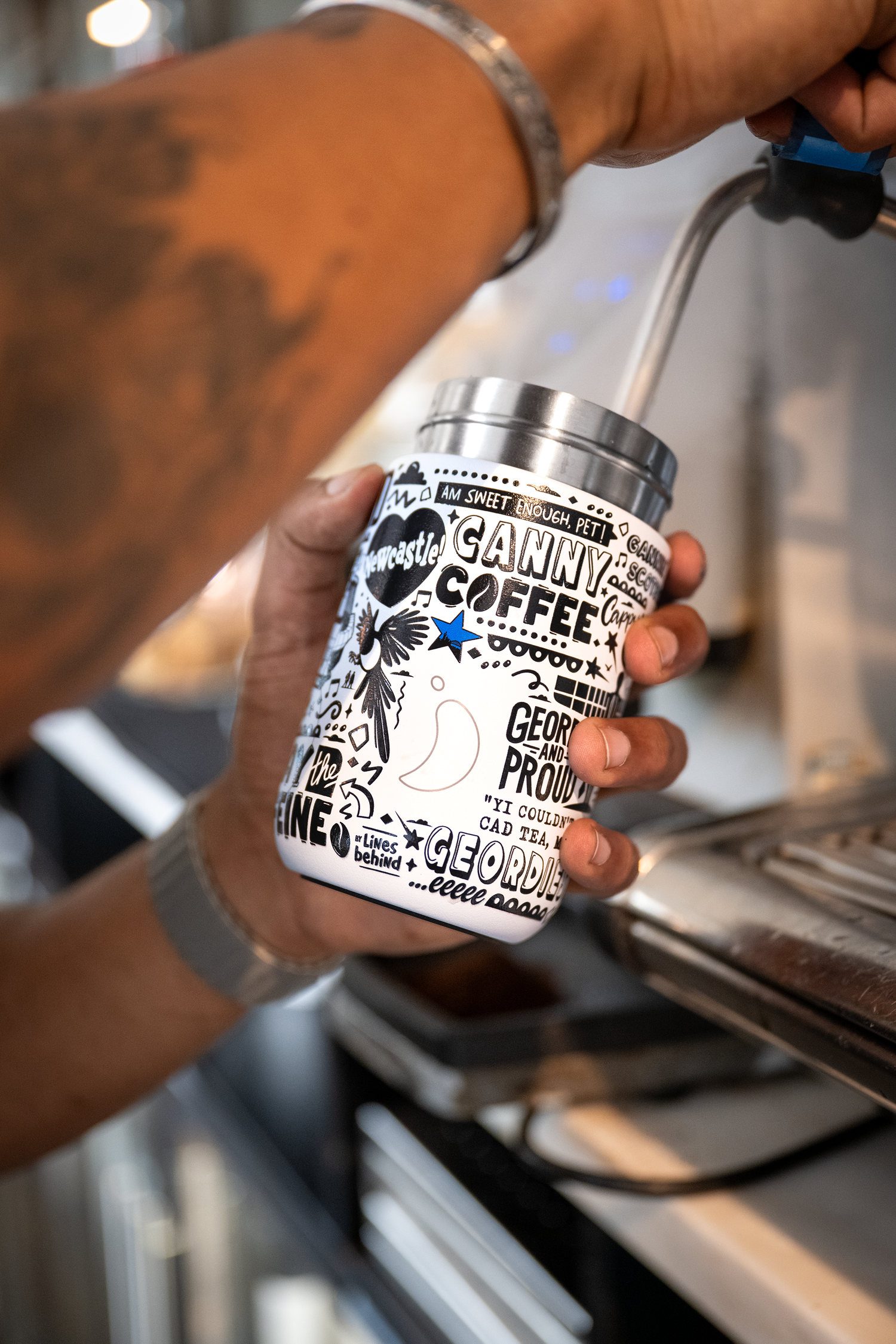 Barista holding a Chilly's coffee cup with a coffee machine in the background