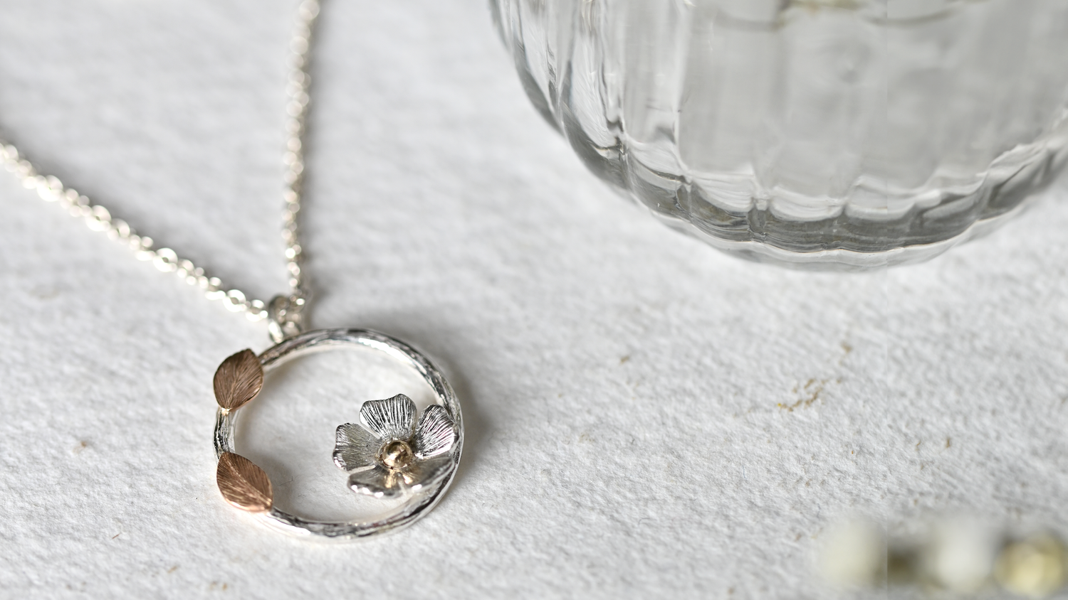 Silver Flower Necklace photographed on a white background with a glass vase in the background