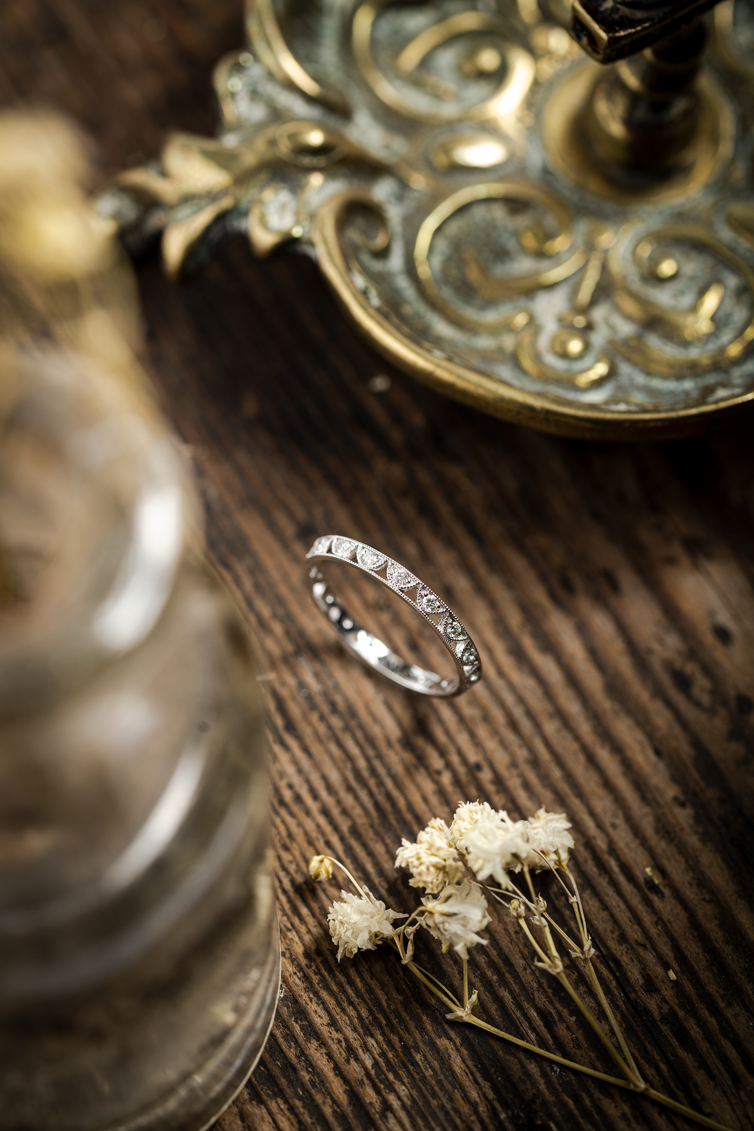 Vintage bevelled diamond eternity ring photographed on a wooden backdrop along with antique looking props and dried flowers